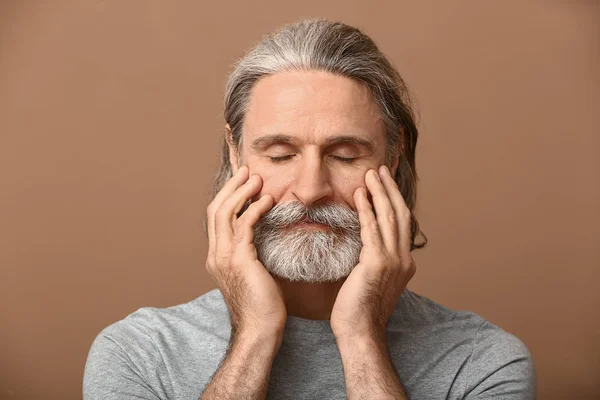 Portrait of mature man touching his face on color background — Stock Photo, Image