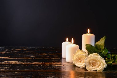 Burning candles and flowers on table against black background clipart