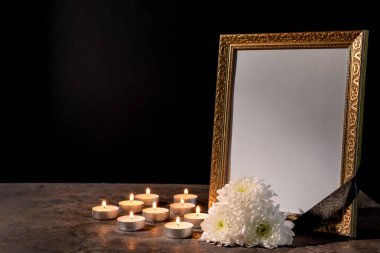 Blank funeral frame, candles and flowers on table against black background clipart