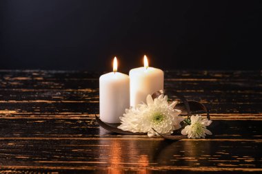 Burning candles and flowers on table against black background clipart