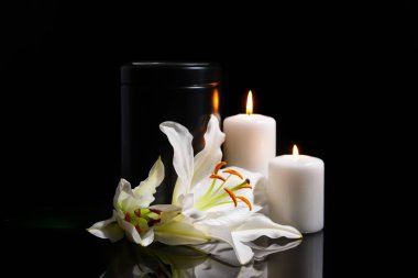 Mortuary urn, burning candles and lily flowers on dark background clipart