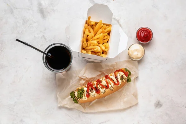 Sabroso perrito caliente con salsas, papas fritas y bebida en la mesa ligera — Foto de Stock