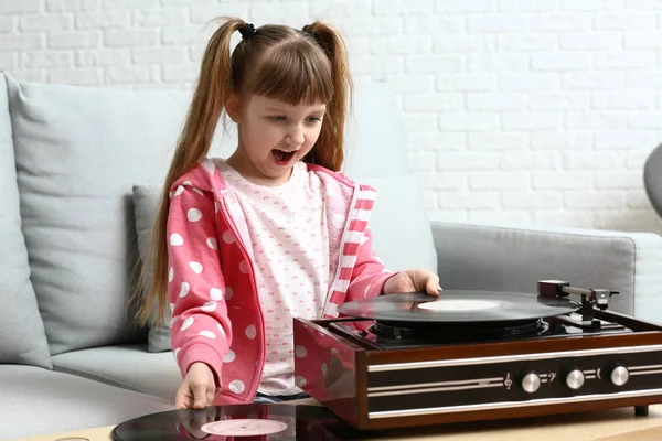 Милая маленькая девочка слушает музыку через музыкальный проигрыватель дома — стоковое фото