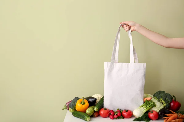 Mão feminina com saco ecológico e legumes frescos na mesa contra fundo de cor — Fotografia de Stock