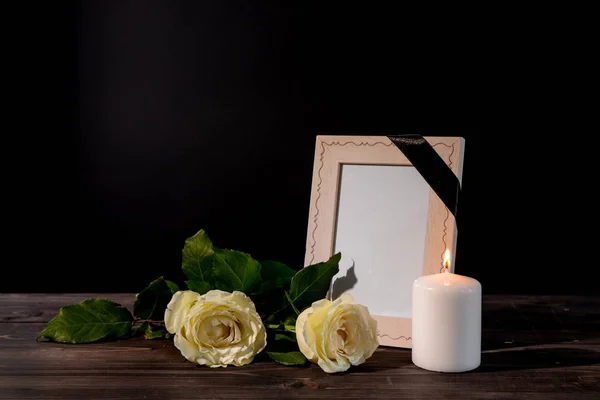 Blank funeral frame, candle and flowers on table against black background — Stock Photo, Image