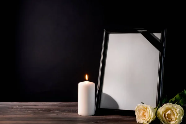 Blank funeral frame, candle and flowers on table against black background — Stock Photo, Image