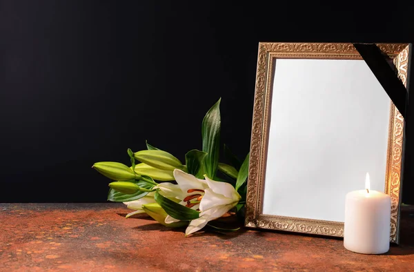 Moldura funerária em branco, vela e flores na mesa contra fundo preto — Fotografia de Stock