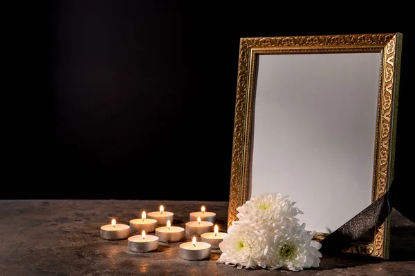 Moldura funerária em branco, velas e flores na mesa contra fundo preto — Fotografia de Stock