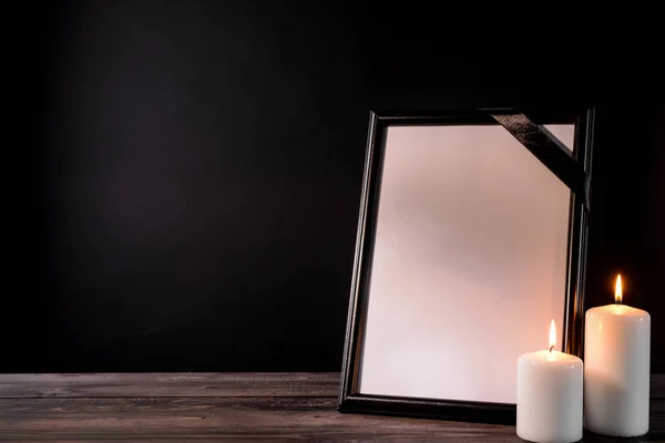 Moldura funerária em branco e velas na mesa contra fundo preto — Fotografia de Stock