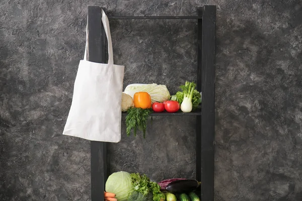 Rack with hanging eco bag and fresh vegetables on grunge background — Stock Photo, Image