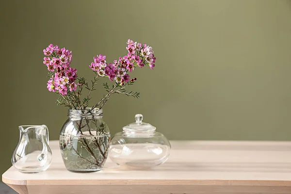 Jar with beautiful flowers on table against color background — Stock Photo, Image