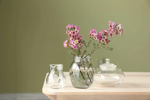 Jar with beautiful flowers on table against color background — Stock Photo, Image