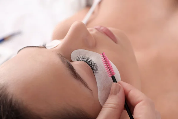 Young woman undergoing eyelash extension procedure in beauty salon, closeup — Stock Photo, Image