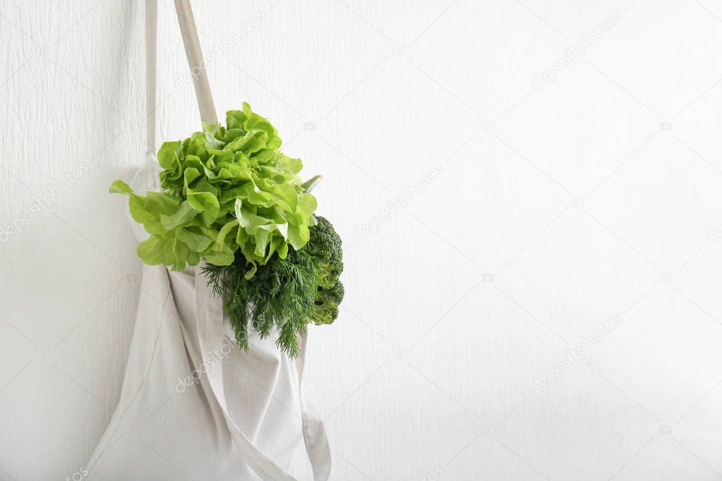 Eco bag with fresh vegetables hanging on wall