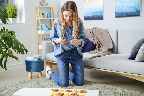 Fotógrafa gastronómica con teléfono móvil tomando fotos de sabrosas galletas y rodajas de naranja en casa —  Fotos de Stock