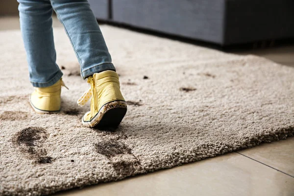 Маленька дівчинка в брудному взутті розбиває килим вдома — стокове фото