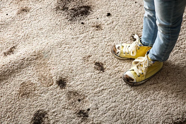 Little girl in muddy shoes messing up carpet at home — Stock Photo, Image