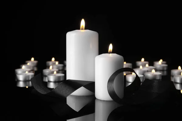 Velas ardientes y cinta de luto sobre fondo negro — Foto de Stock