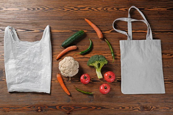 Plastic and fabric bags with fresh vegetables on wooden background. Ecology concept