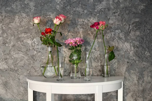 Jarrones de vidrio con hermosas flores en la mesa cerca de la pared grunge —  Fotos de Stock