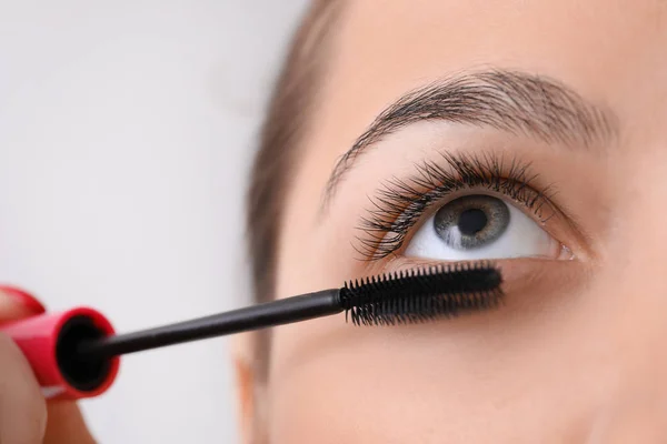 Mooie jonge vrouw met wimper extensions toepassing van mascara op lichte achtergrond, close-up — Stockfoto