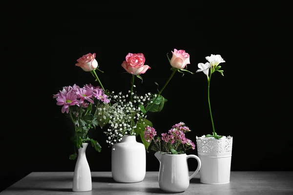 Vasen mit schönen Blumen auf dem Tisch vor dunklem Hintergrund — Stockfoto