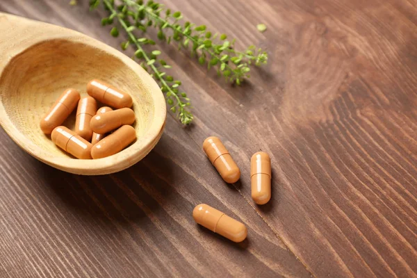 Colher com pílulas à base de plantas em fundo de madeira — Fotografia de Stock