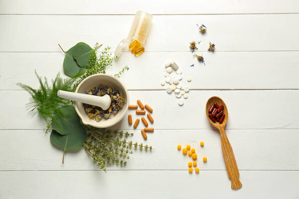 Composition with mortar, herbs and plant based pills on white wooden background