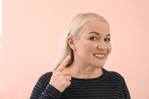 Ώριμη γυναίκα με ακουστικό βαρηκοΐας στο χρώμα φόντου — Φωτογραφία Αρχείου