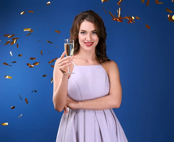 Beautiful young woman with glass of champagne and falling confetti on color background — Stock Photo, Image