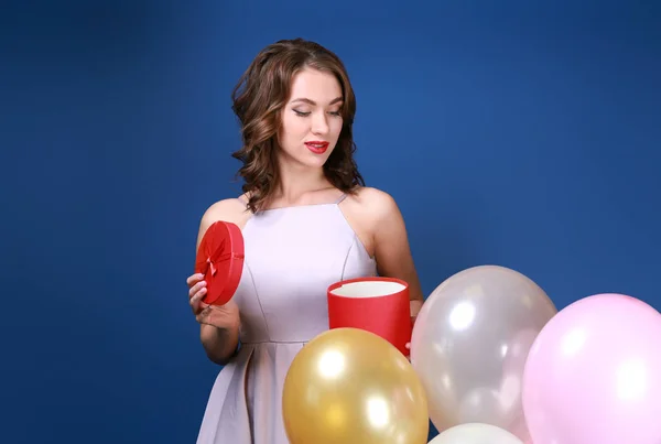 Beautiful young woman with balloons and gift on color background — Stock Photo, Image