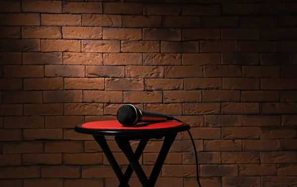 Moderní mikrofon na stoličce proti cihlové pozadí — Stock fotografie