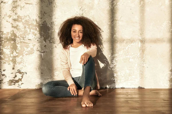 Belle femme afro-américaine assise sur le sol près du mur de grunge — Photo