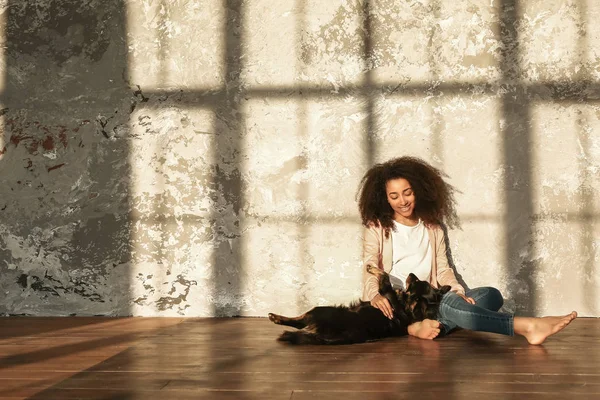 Hermosa mujer afroamericana con lindo perro sentado en el suelo cerca de la pared grunge —  Fotos de Stock