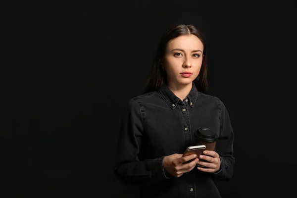 Elegante mujer de negocios con taza de café y teléfono móvil sobre fondo oscuro —  Fotos de Stock