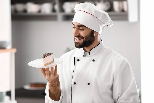 Confeiteiro masculino com pedaço de bolo saboroso na cozinha — Fotografia de Stock