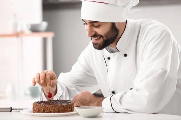 Mannelijke banketbakker versieren van lekkere chocolade cake in keuken — Stockfoto