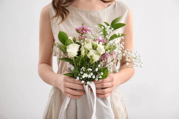 Young woman with bouquet of flowers in eco bag on light background — Stock Photo, Image