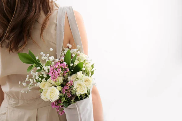 Young woman with bouquet of flowers in eco bag on light background — Stock Photo, Image