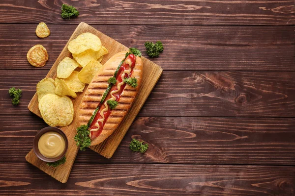 Board with tasty hot dog on wooden background — Stock Photo, Image