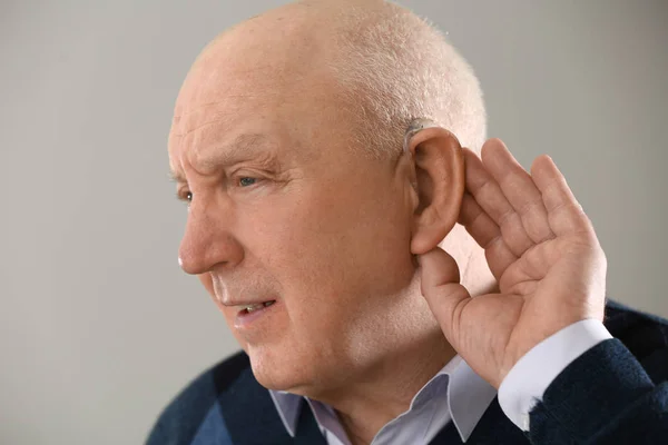 Senior man with hearing aid on light background — Stock Photo, Image
