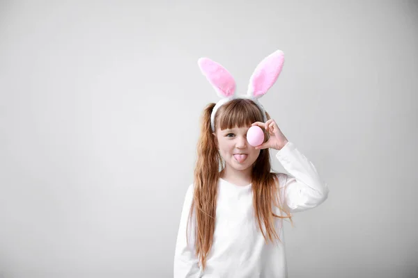 Cute little girl with Easter egg and bunny ears on light background — Stock Photo, Image