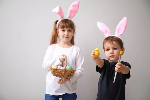 Crianças pequenas bonitos com ovos de Páscoa e orelhas de coelho no fundo claro — Fotografia de Stock