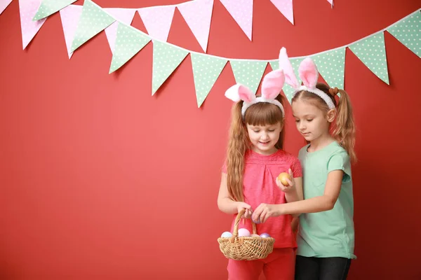 Cute little girls with Easter eggs and bunny ears near color decorated wall — Stock Photo, Image