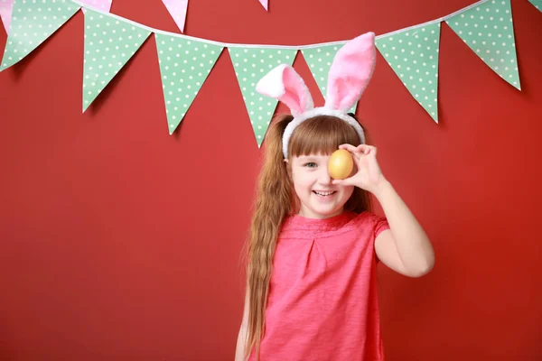 Cute little girl with Easter egg and bunny ears near color decorated wall — Stock Photo, Image