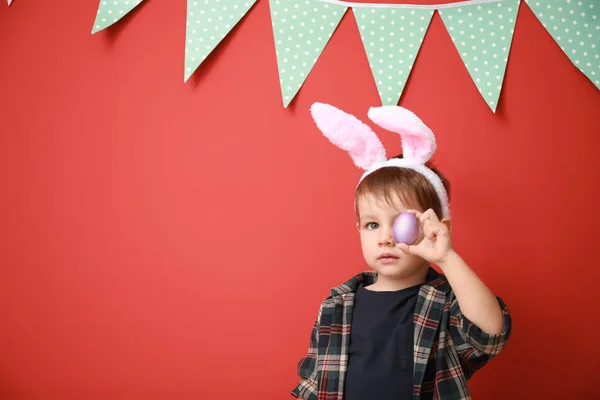 Paskalya yumurtası ve tavşan kulakları dekore edilmiş renk duvarının yakınında şirin küçük çocuk — Stok fotoğraf