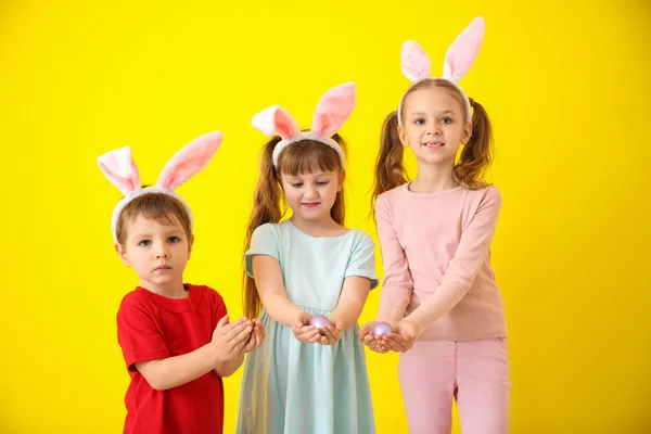 Niedliche kleine Kinder mit Ostereiern und Hasenohren auf farbigem Hintergrund — Stockfoto