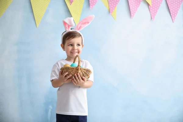 Niedliche kleine Junge mit Ostereiern und Hasenohren in der Nähe Farbe dekorierte Wand — Stockfoto