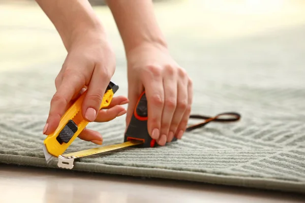 Woman with tape measure cutting carpet on floor, closeup — Stock Photo, Image