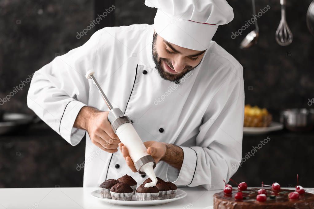 Male confectioner cooking tasty cupcakes in kitchen